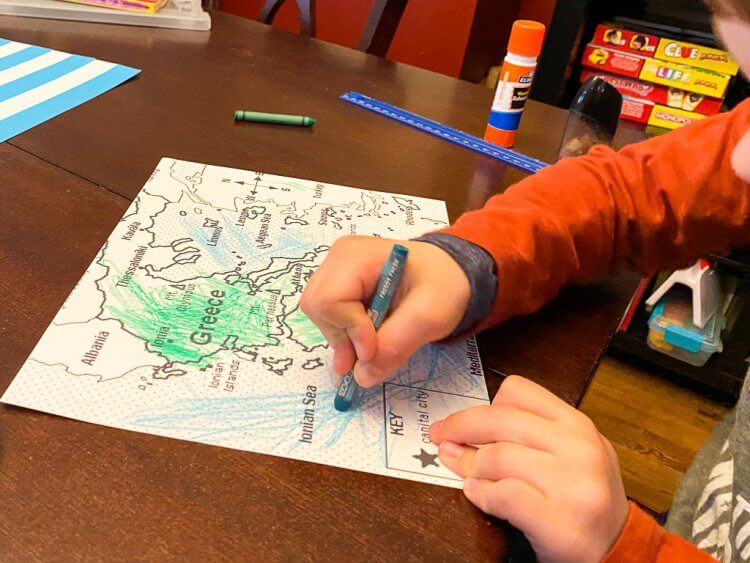 Boy with orange shirt coloring a map of Greece.