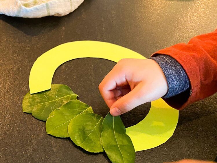 Gluing the leaves to a ring made out of paper to form a wreath.