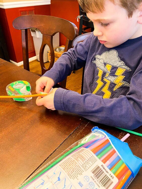 Little boy constructing a straw bridge with tape.