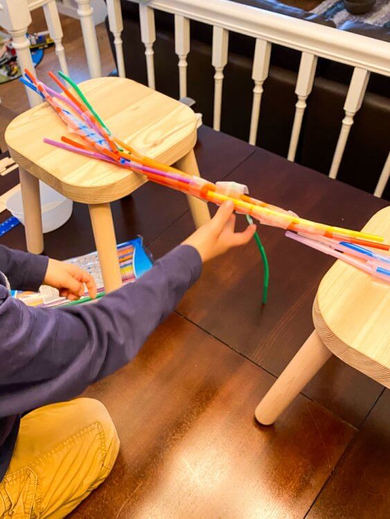 Little boy constructing a straw bridge with tape.