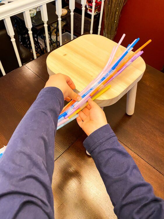 Little boy constructing a straw bridge with tape.