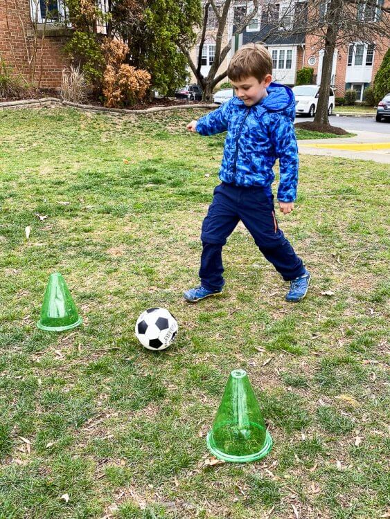 Little boy in an owl coat kicking a soccer ball between to cones.