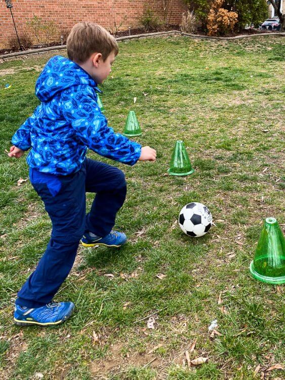 Little boy in an owl coat kicking a soccer ball between to cones.