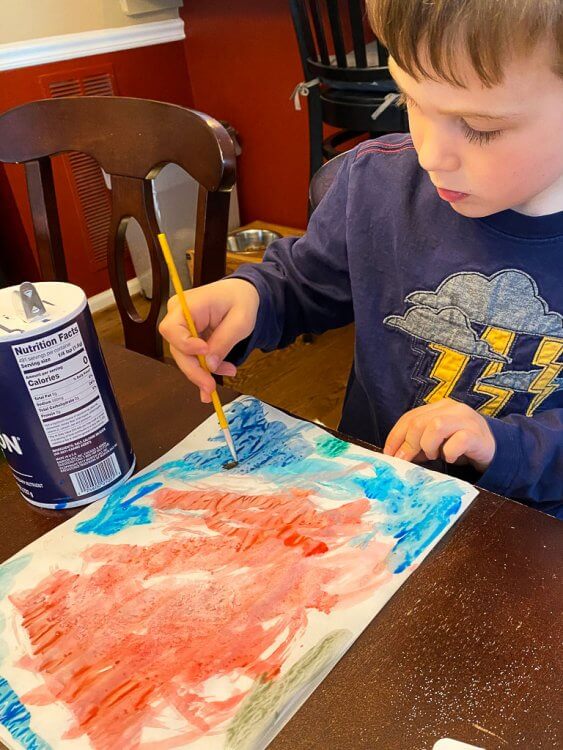 Little boy coloring with watercolors at the dining room table.