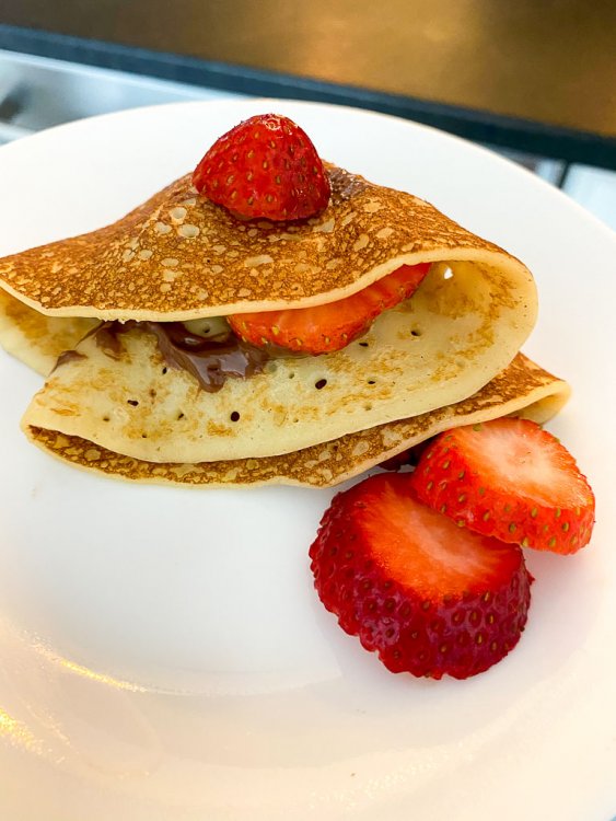 Finished crepe folded on a plate with nutella and strawberries.
