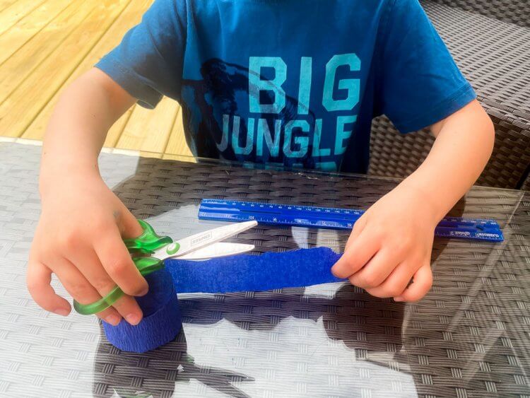 Little boy cutting crepe paper into 12 inch strips.