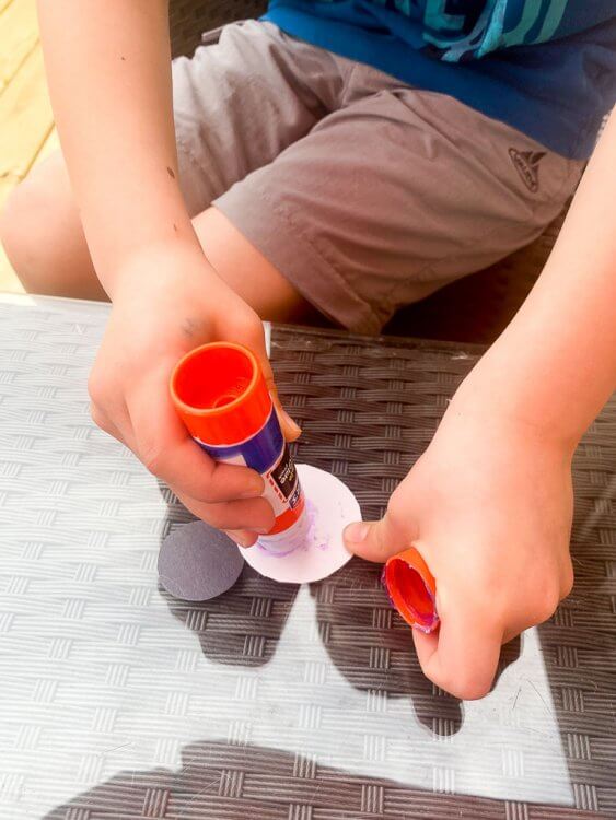 Little boy gluing black dots to white paper circles.