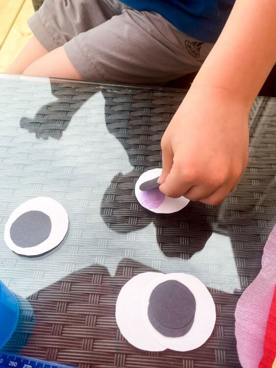Little boy gluing black dots to white paper circles.