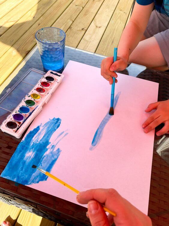 Using blue watercolors to paint a background on white paper.