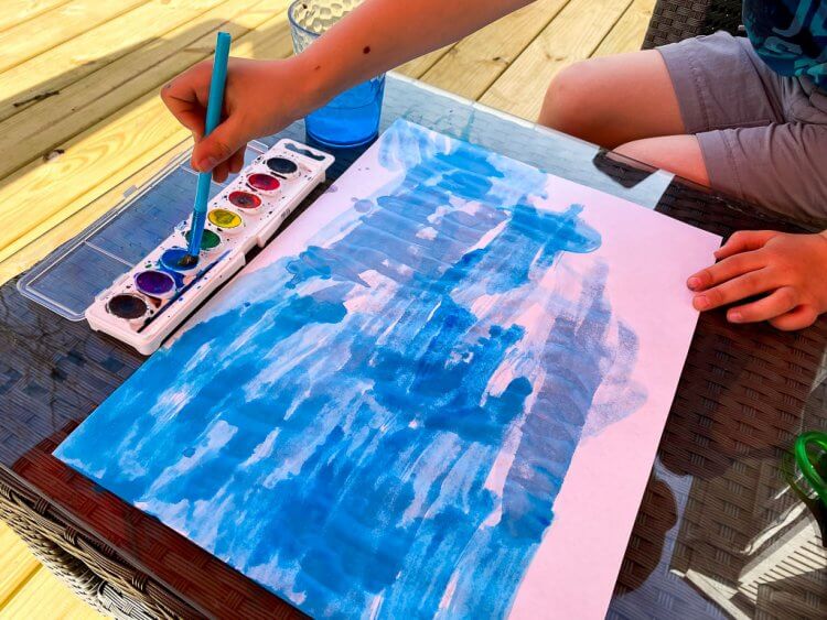 Using blue watercolors to paint a background on white paper.