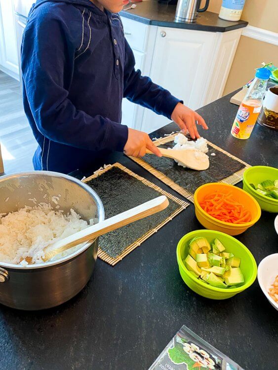 Little boy putting a scoop of rice on his seaweed.