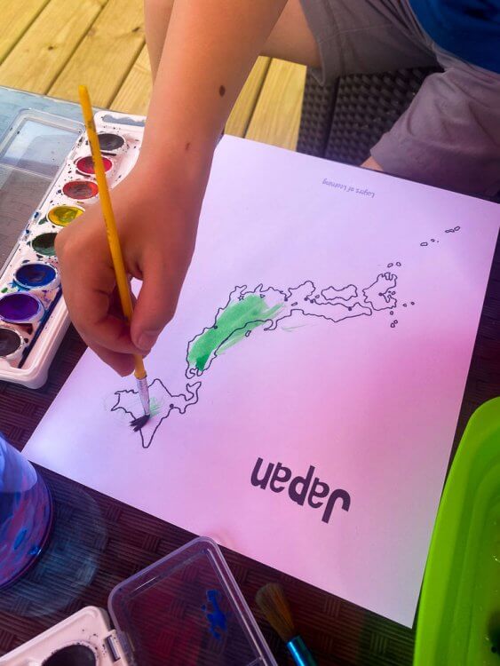 Little boy painting a map of Japan with green watercolors.